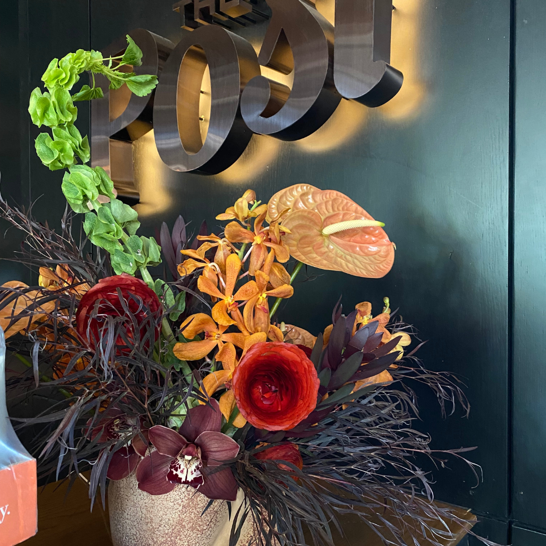 Large flower arrangement at The Post Tavern in the Ada Hotel. Subdued fall color palette with pops of orange orchids and a bright green sprig of Bells of Irelan