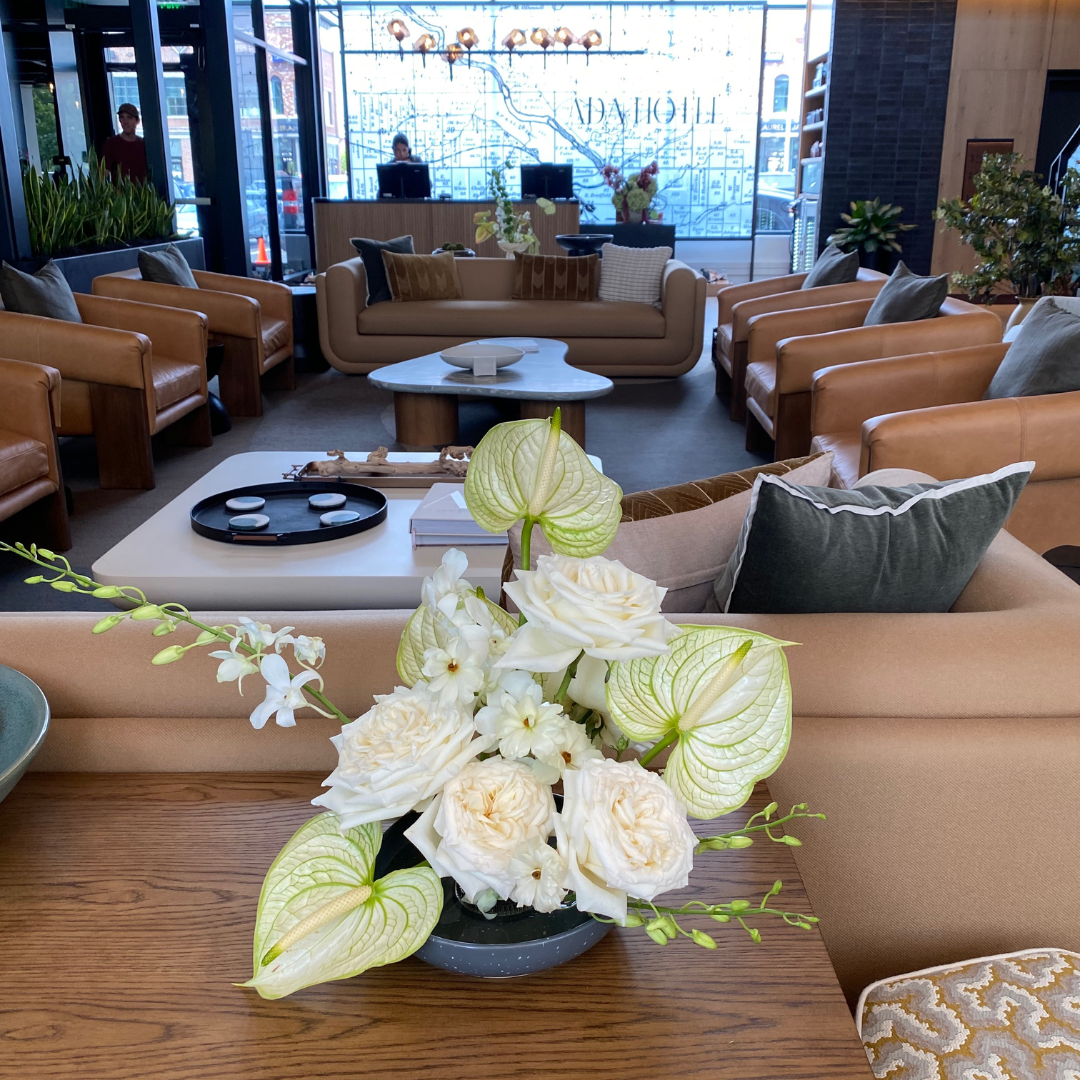 White roses, white and green anthruium and white orchids on a common area table in the Ada Hotel