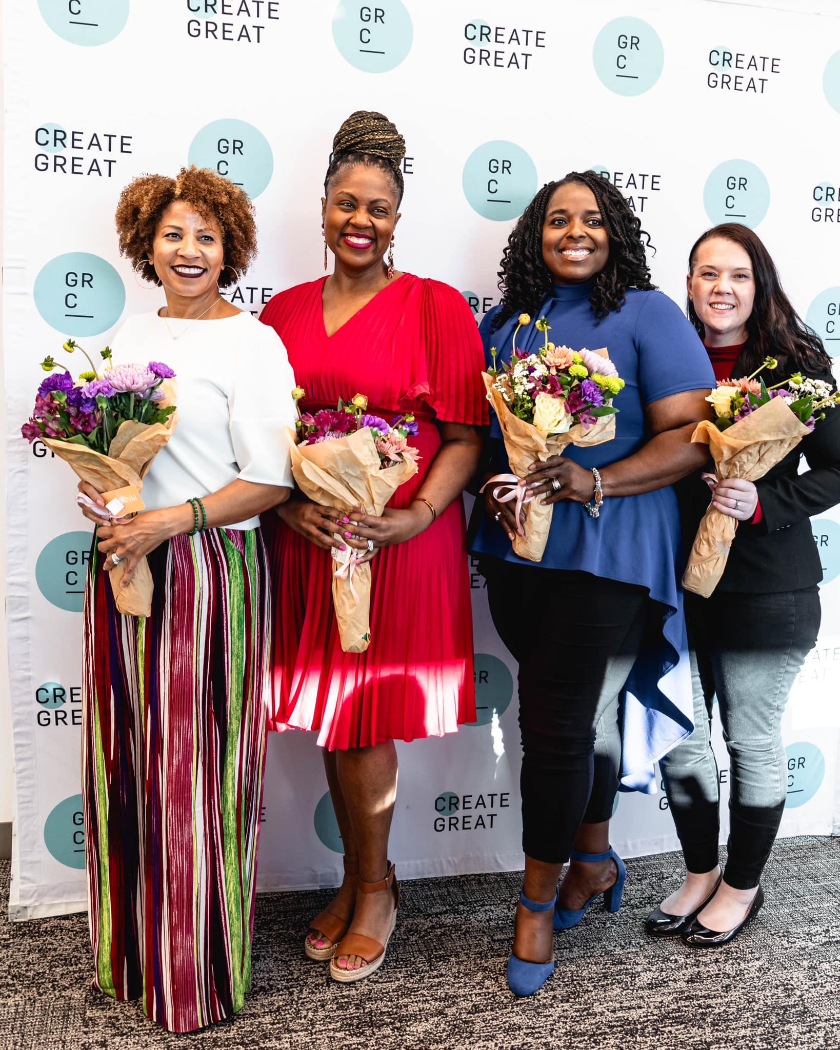 Award winners holding colorful flower bouquets at a corporate event at the Grand Rapids Chamber