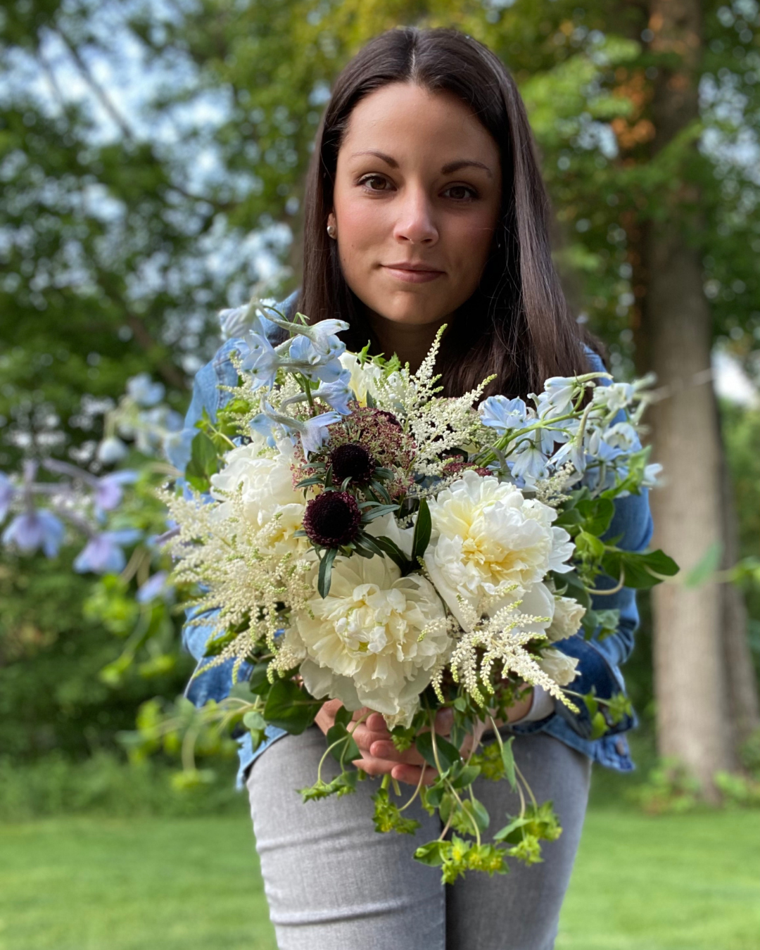 Floral designer showing off large wedding bouquet with peonies, delphinium, bupleurum, scabiosa and astillbe.