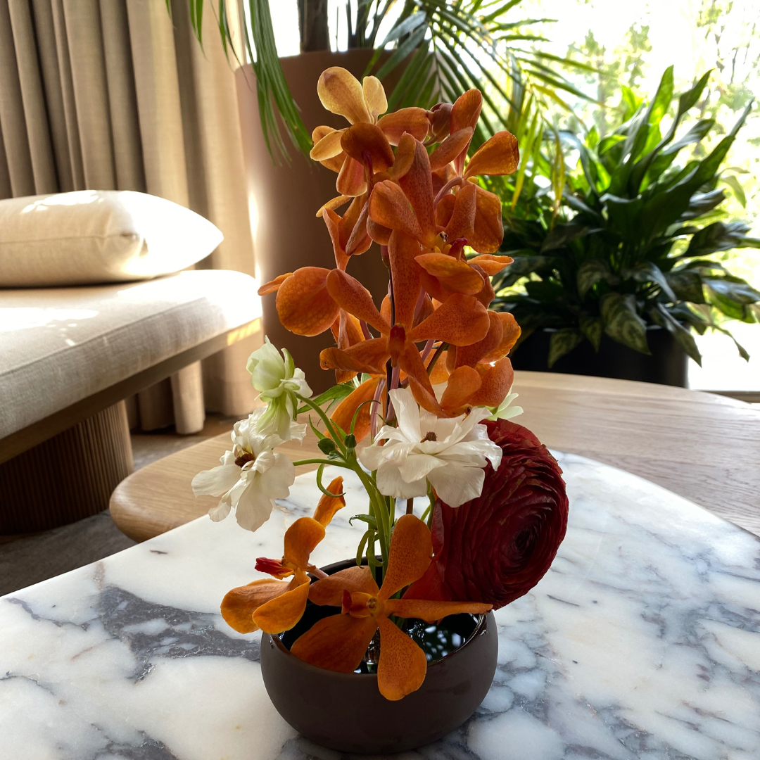 orange orchids as the focal flower in a small floral arrangement on a side table in hotel common area